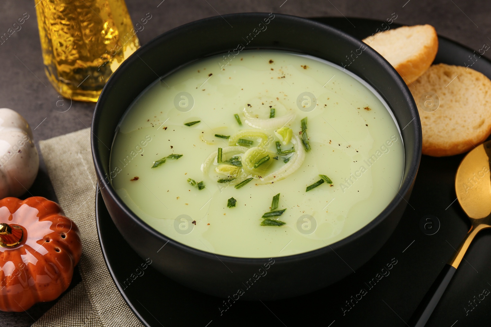 Photo of Bowl of tasty leek soup, spoon and bread on grey table, closeup