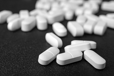 Photo of Many white pills on dark surface, closeup