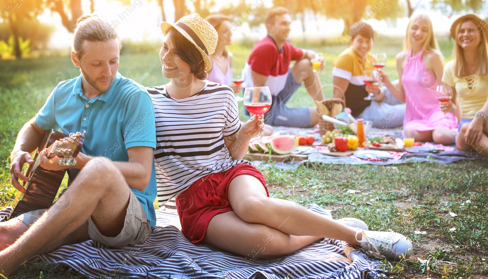 Image of Young man playing guitar for his girlfriend in park. Summer picnic