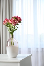 Vase with beautiful alstroemeria flowers on table near window indoors. Stylish element of interior design