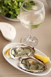 Photo of Plate of delicious raw oysters served with lemon and wine at wooden table