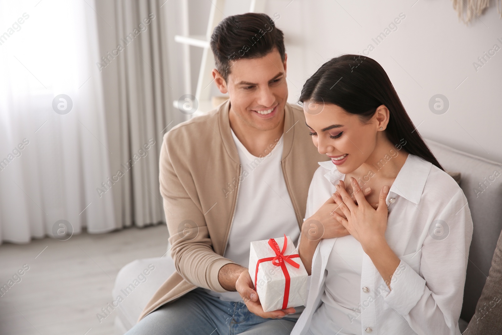 Photo of Man presenting gift to his beloved woman at home. Valentine's day celebration