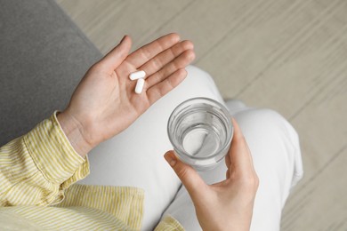 Calcium supplement. Woman holding glass of water and pills indoors, top view