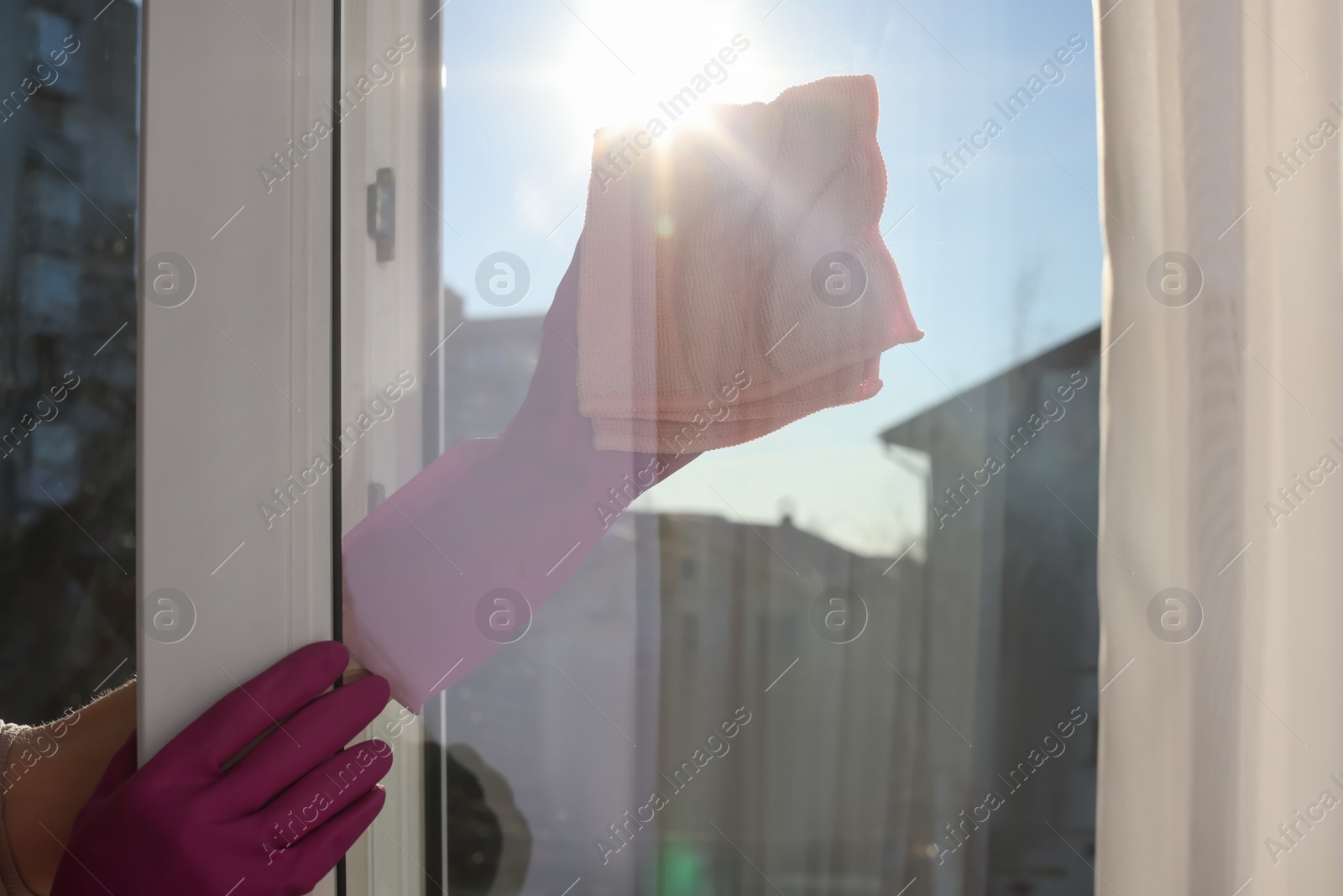 Photo of Young woman cleaning window glass with rag at home, closeup