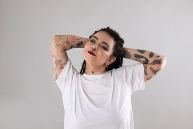 Photo of Beautiful young woman with tattoos on arms, nose piercing and dreadlocks against grey background