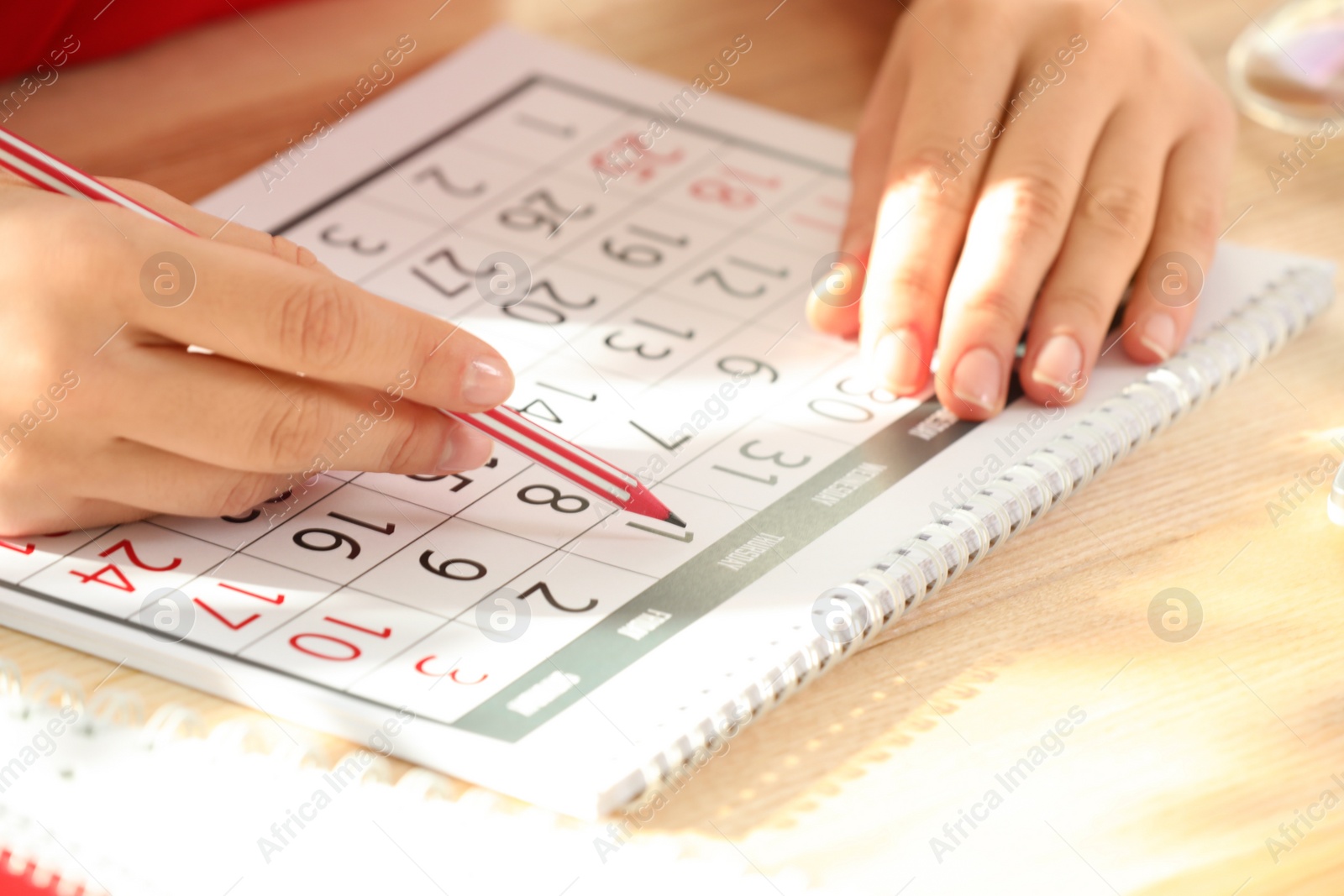 Photo of Woman marking date in calendar at wooden table, closeup