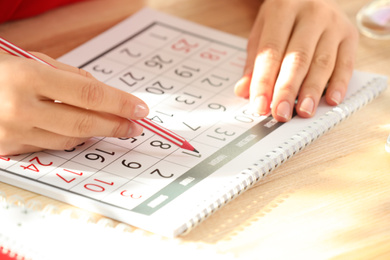 Woman marking date in calendar at wooden table, closeup