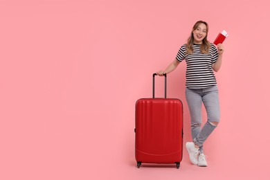 Photo of Happy young woman with passport, ticket and suitcase on pink background, space for text