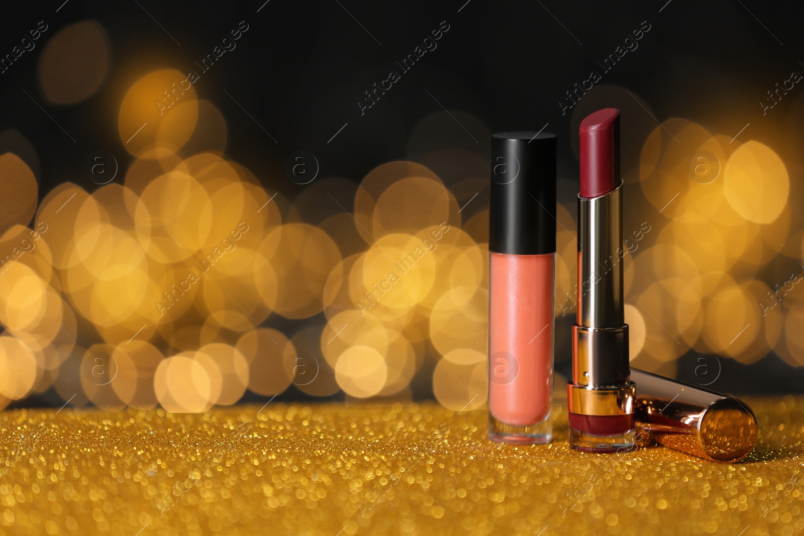 Photo of Bright lipsticks on table with gold glitter against blurred lights, space for text