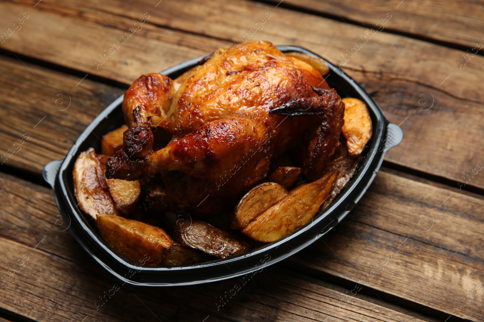 Photo of Delicious grilled chicken with potato in plastic container on wooden table. Food delivery service