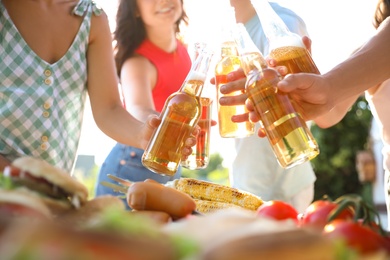 Photo of Friends toasting with bottles of beer outdoors, closeup. Camping season