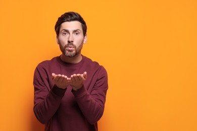 Photo of Handsome man blowing kiss on orange background. Space for text