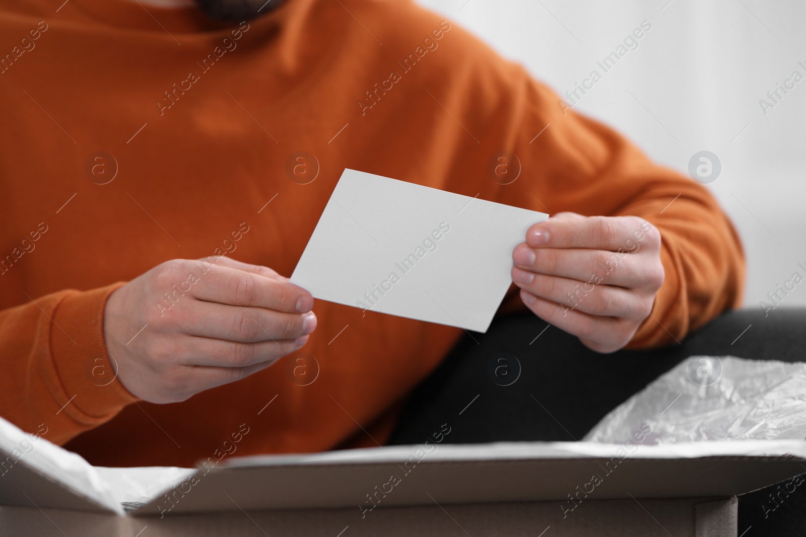 Photo of Man holding greeting card near parcel with Christmas gift, closeup