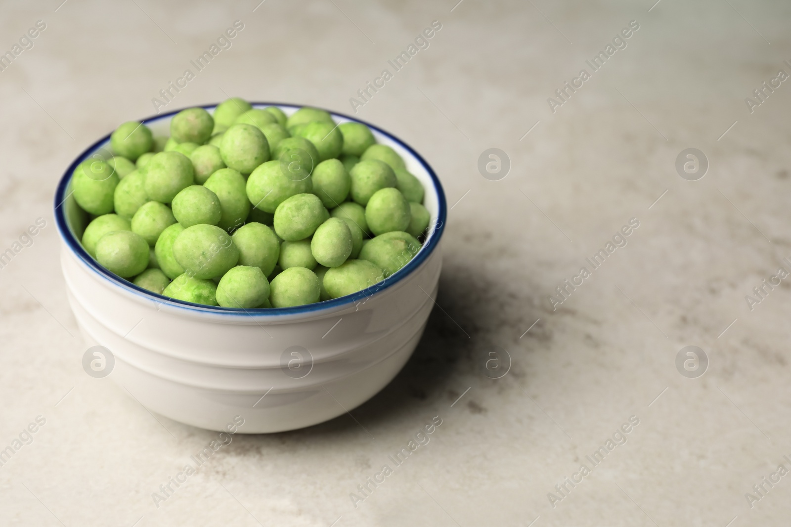 Photo of Tasty wasabi coated peanuts in bowl on table, space for text