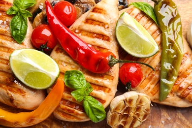 Tasty grilled chicken fillets with vegetables and lime slices on wooden board, closeup