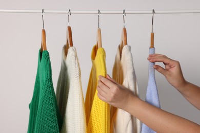 Photo of Woman taking sweater from rack on light background, closeup
