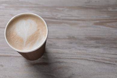 Photo of To-go drink. Tasty coffee in paper cup on light wooden table, above view. Space for text