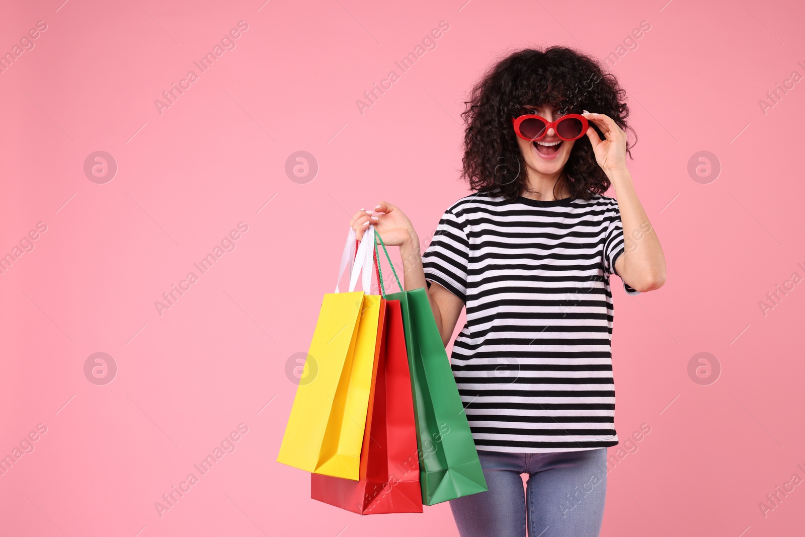 Photo of Happy young woman with shopping bags and stylish sunglasses on pink background. Space for text