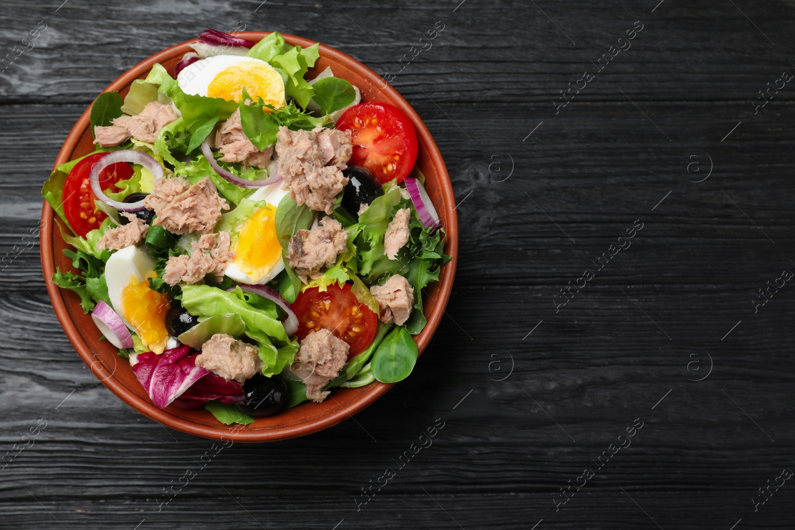 Photo of Bowl of delicious salad with canned tuna and vegetables on black wooden table, top view. Space for text