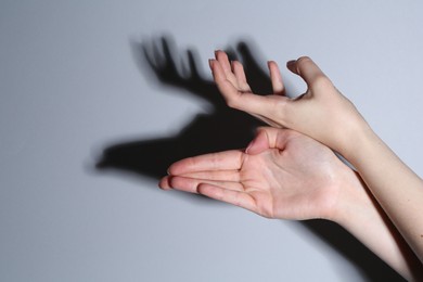 Photo of Shadow puppet. Woman making hand gesture like deer on grey background, closeup
