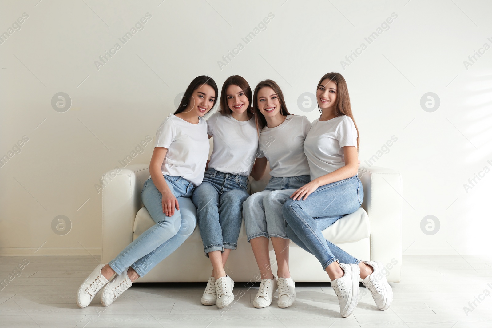 Photo of Beautiful young ladies in jeans and white t-shirts on sofa indoors. Woman's Day