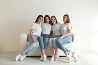 Beautiful young ladies in jeans and white t-shirts on sofa indoors. Woman's Day