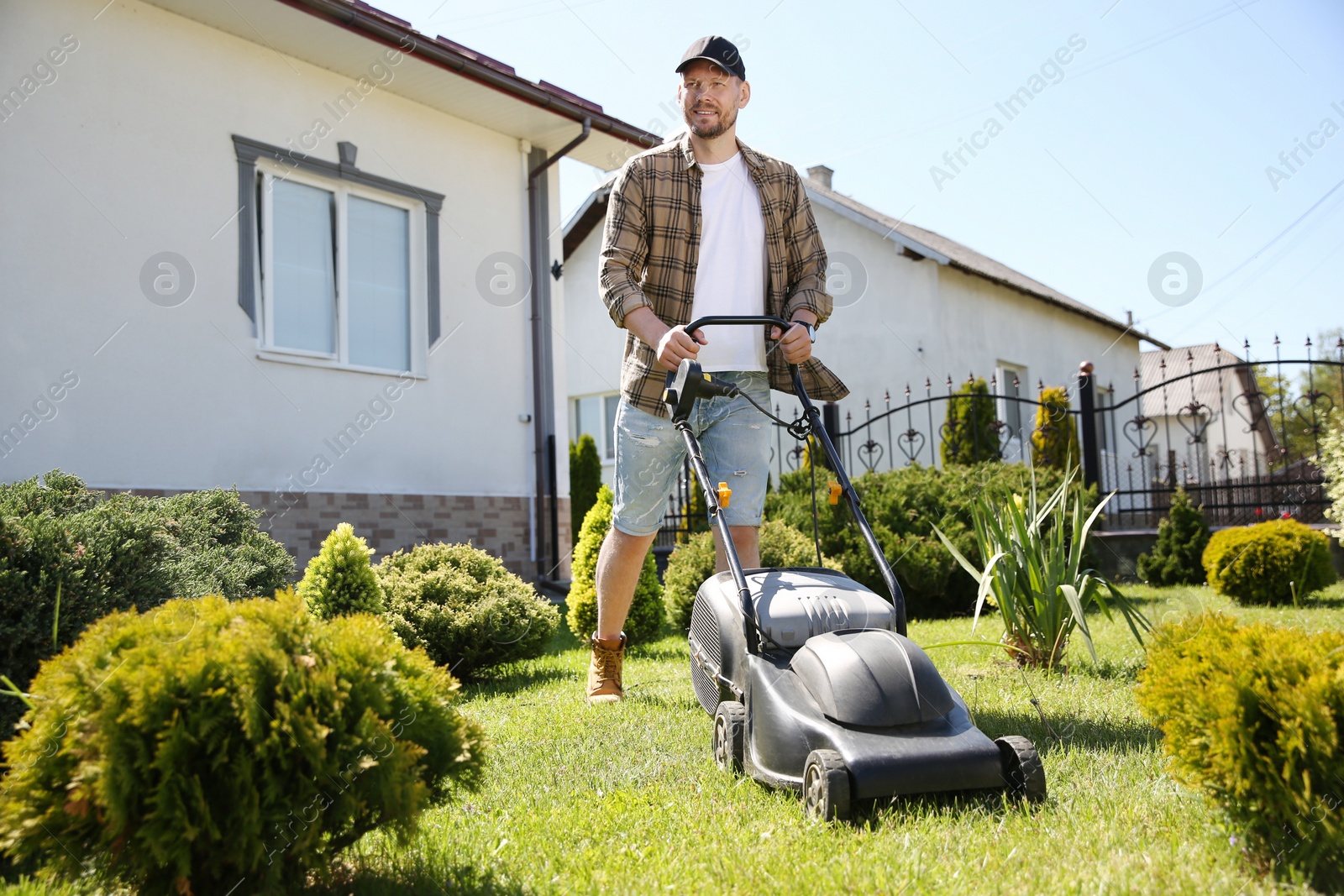 Photo of Man cutting green grass with lawn mower in garden