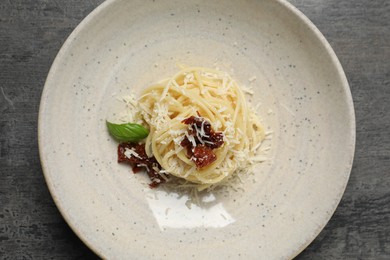Photo of Tasty spaghetti with sun-dried tomatoes and parmesan cheese on grey table, top view. Exquisite presentation of pasta dish