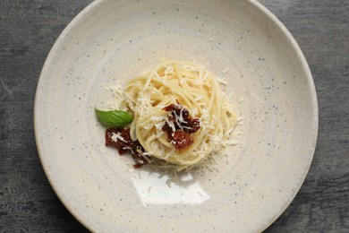 Tasty spaghetti with sun-dried tomatoes and parmesan cheese on grey table, top view. Exquisite presentation of pasta dish