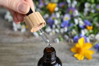 Photo of Woman pouring essential oil from pipette into bottle on table, closeup