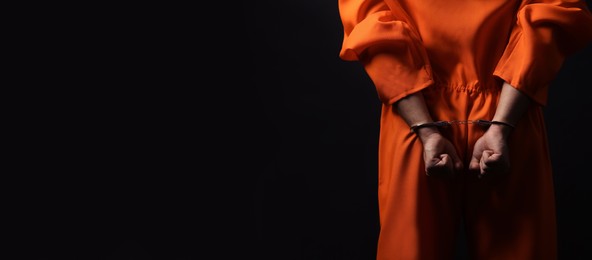 Photo of Prisoner in jumpsuit with handcuffs on black background, closeup. Space for text