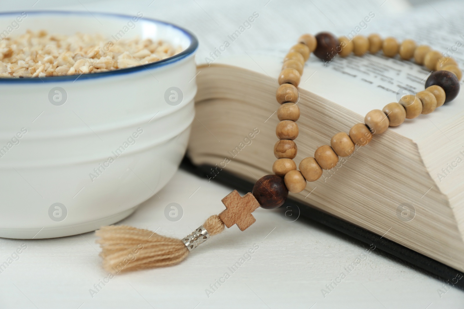 Photo of Oatmeal, rosary beads and Bible on white table, closeup. Lent season