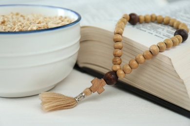 Photo of Oatmeal, rosary beads and Bible on white table, closeup. Lent season