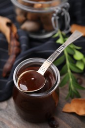 Photo of Jar of tasty tamarind sauce, spoon and fresh pods on wooden table