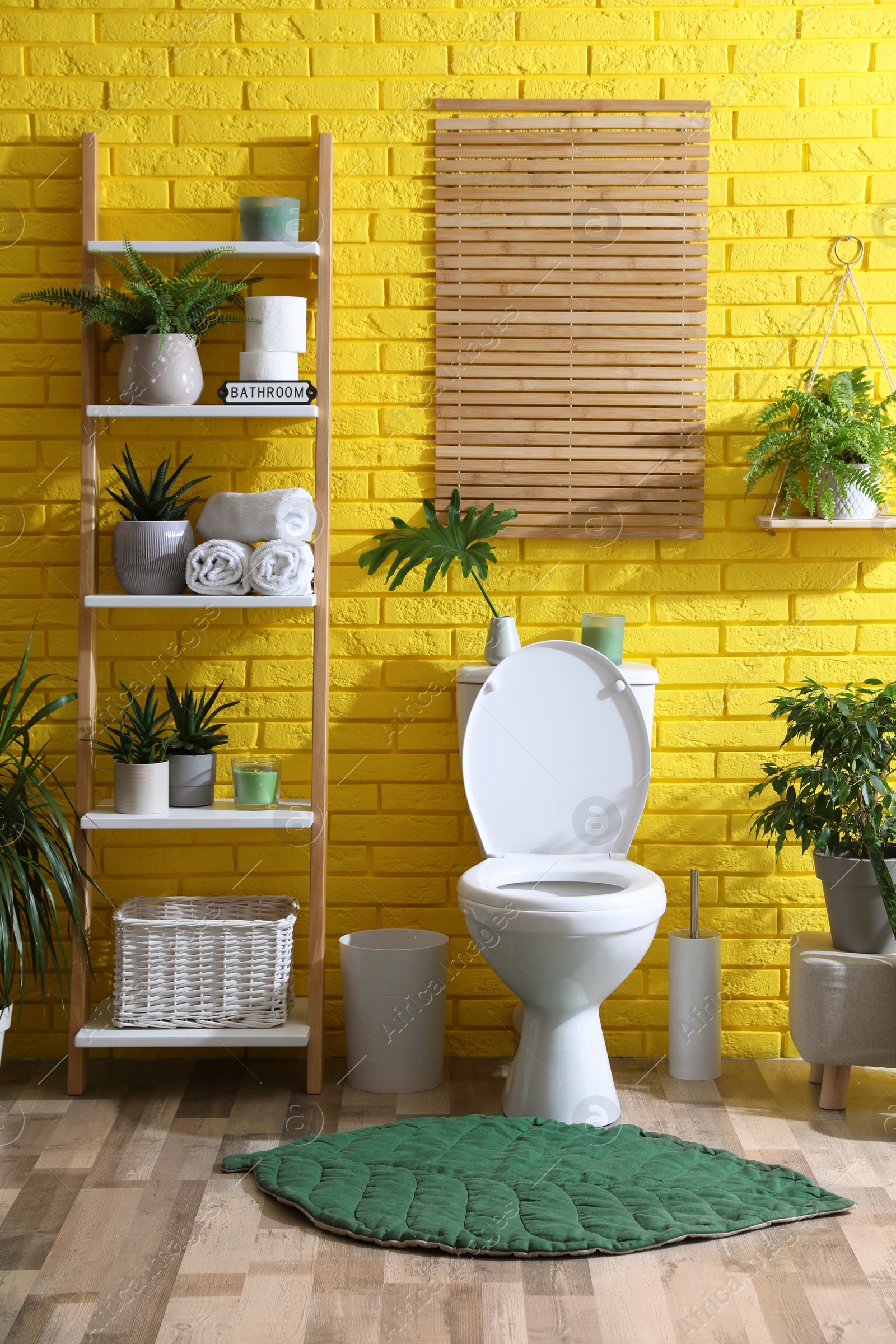 Photo of Stylish bathroom with toilet bowl and green plants near yellow brick wall. Interior design