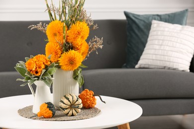 Photo of Beautiful autumn bouquets and pumpkins on coffee table near sofa in room