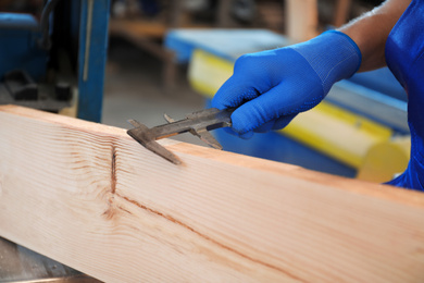 Photo of Professional carpenter measuring wooden board with sliding caliper in workshop, closeup