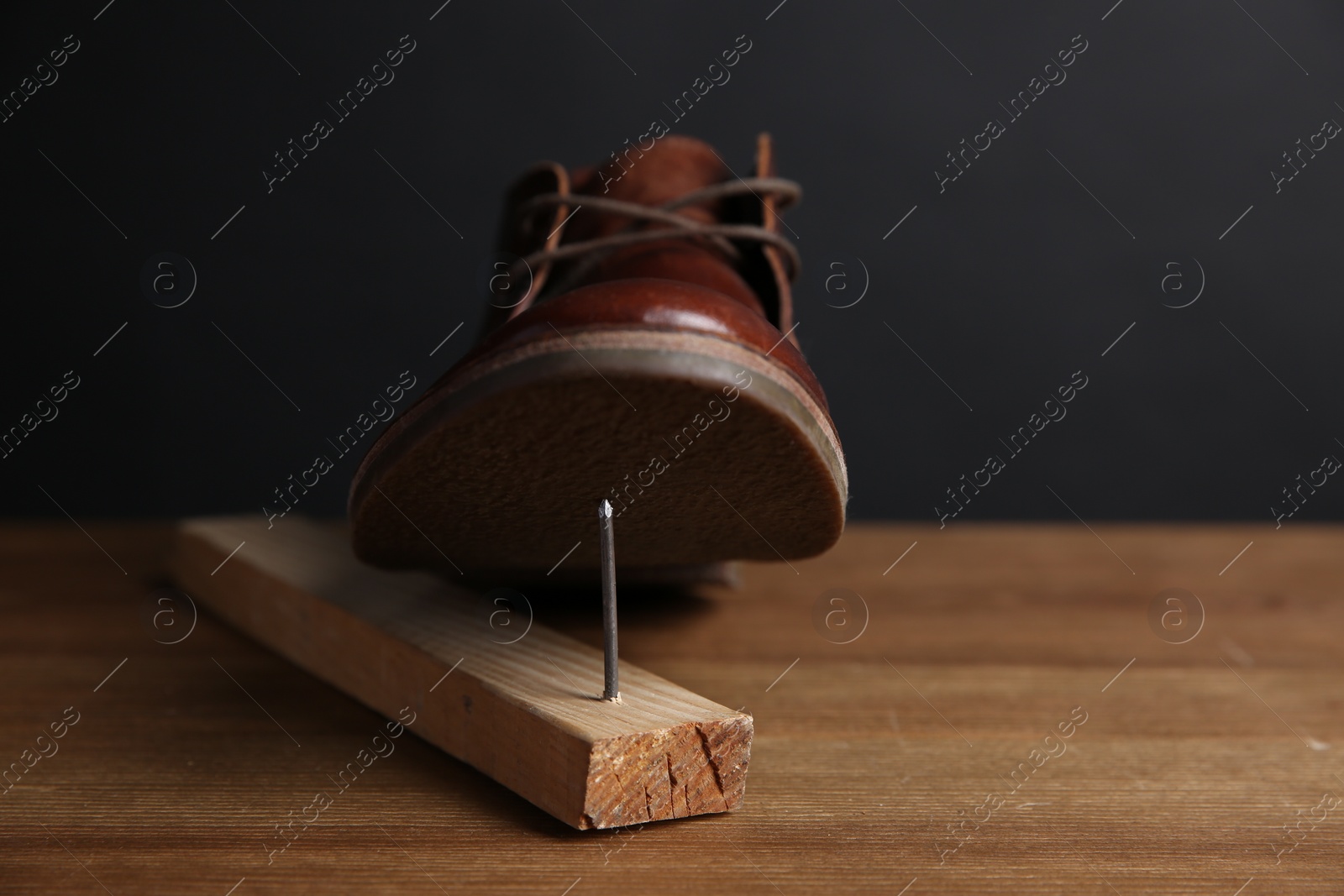 Photo of Metal nail in wooden plank and shoes on table, closeup