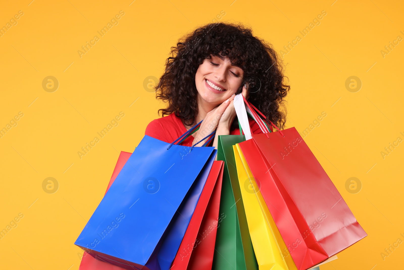 Photo of Happy young woman with shopping bags on yellow background