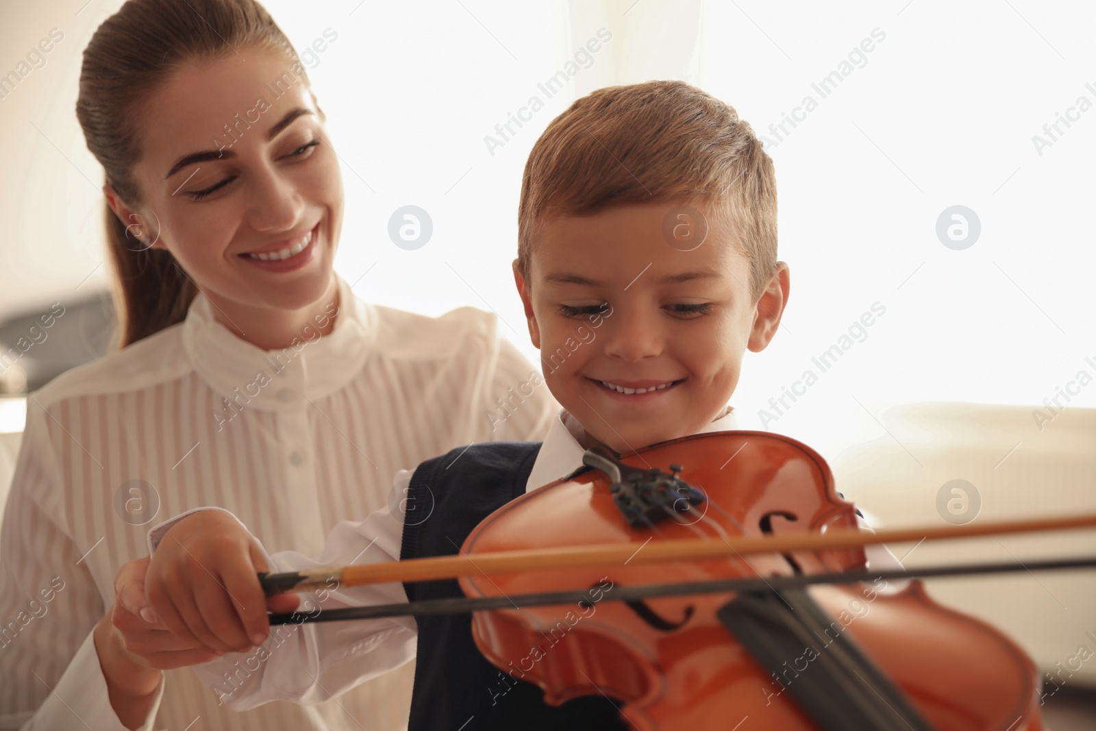 Photo of Young woman teaching little boy to play violin indoors