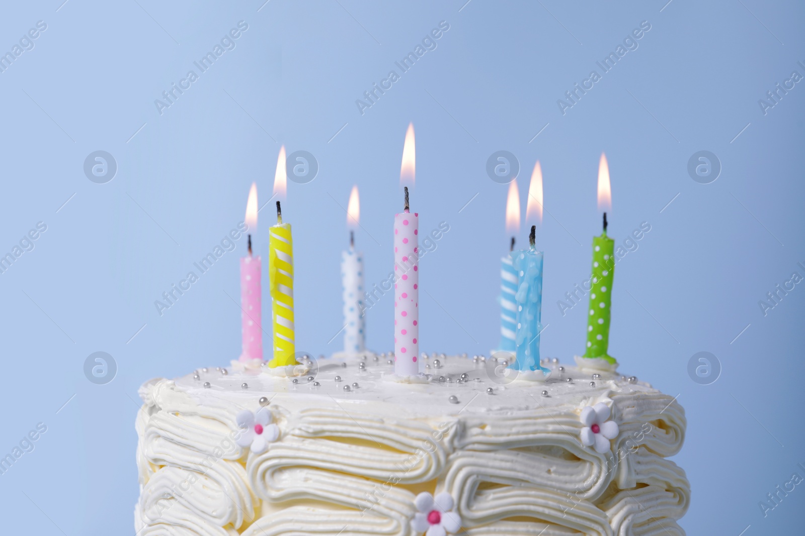 Photo of Delicious cake with cream and burning candles on light blue background, closeup