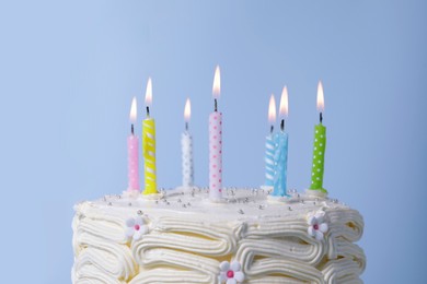 Delicious cake with cream and burning candles on light blue background, closeup