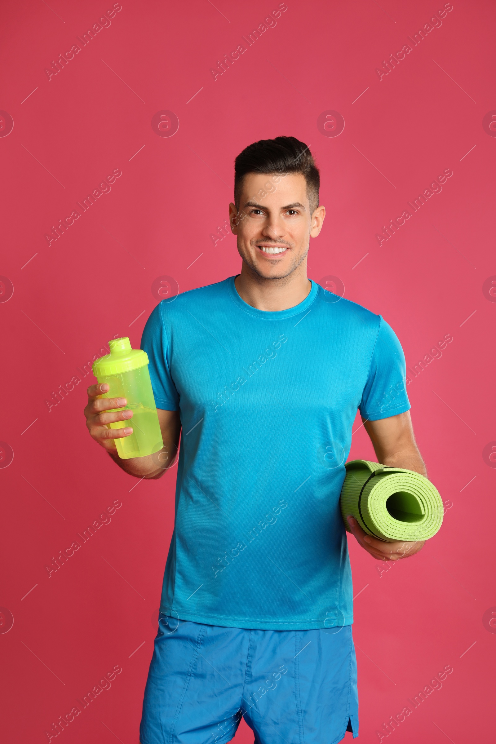 Photo of Handsome man with yoga mat and shaker on pink background