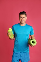 Handsome man with yoga mat and shaker on pink background