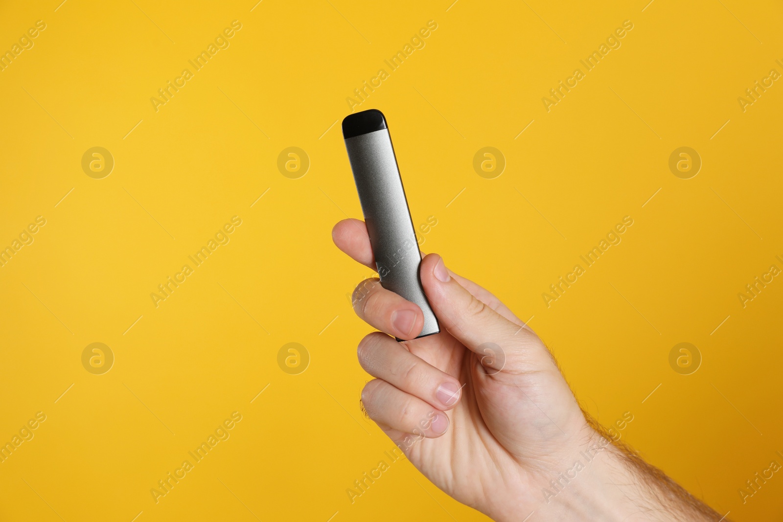 Photo of Man holding electronic cigarette on yellow background, closeup