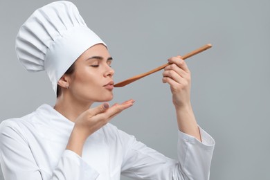 Photo of Happy female chef tasting something on light grey background