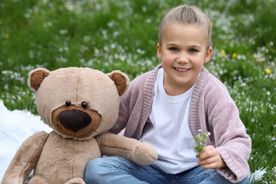 Little girl with teddy bear on plaid outdoors