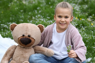 Photo of Little girl with teddy bear on plaid outdoors