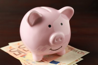 Ceramic piggy bank and banknotes on wooden table, closeup