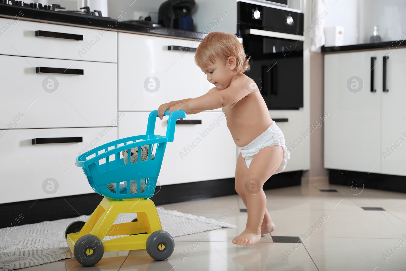 Photo of Cute baby with toy walker in kitchen. Learning to walk